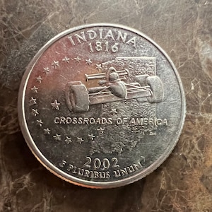 May include: Silver US quarter dollar coin featuring a race car and the text "Indiana 1816 Crossroads of America 2002 E Pluribus Unum".
