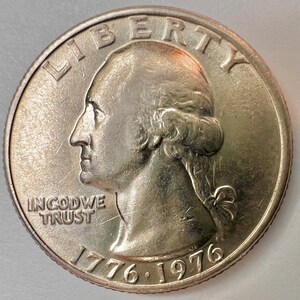 May include: A silver US quarter dollar coin with the profile of George Washington on the obverse. The coin has the inscription "LIBERTY" above the profile and "IN GOD WE TRUST" below. The date "1776-1976" is inscribed on the bottom of the coin.