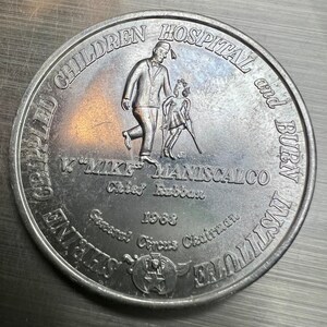 May include: A silver coin with the inscription "Children's Hospital and Burn Institutes" and "W. "Mike" Maniscalco Chief Rabban 1968 General Circus Chairman". The coin features a relief image of a man and a girl walking together.
