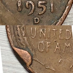 May include: Close-up of a copper coin fragment. The year "1951" and the letter "D" are visible. The words "UNITED OF AM" are also partially visible. The coin has a worn, aged appearance.