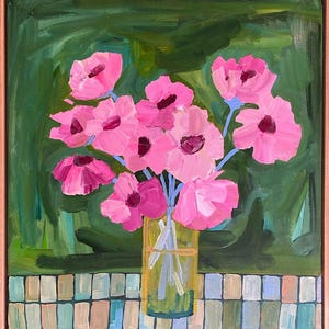 May include: An original painting of pink flowers in a yellow vase. The flowers have dark pink centers and light blue stems. The background is green, and the painting is framed in a light brown frame. The painting is on a mosaic tile surface.