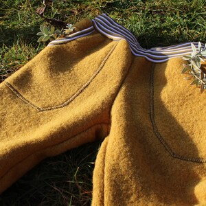 May include: Mustard yellow fleece pants with a white and brown striped waistband and a small red label with the word "Herz" on it.