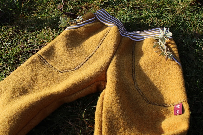 May include: Mustard yellow fleece pants with a white and brown striped waistband and a small red label with the word "Herz" on it.