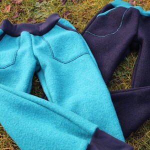 May include: Two pairs of fleece pants, one teal blue and one navy blue. Both pairs have a contrasting black waistband and cuffs. Each pair has a patch pocket on the front with a small red label.