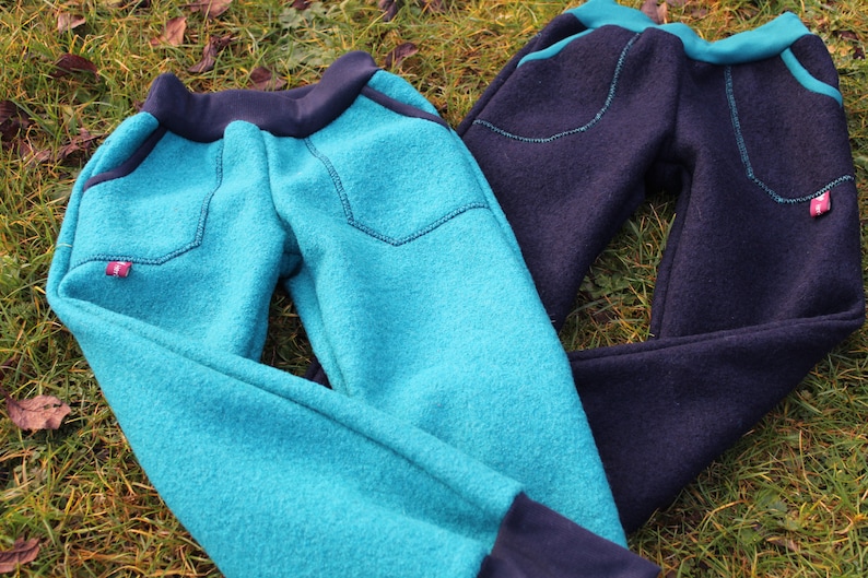 May include: Two pairs of fleece pants, one teal blue and one navy blue. Both pairs have a contrasting black waistband and cuffs. Each pair has a patch pocket on the front with a small red label.