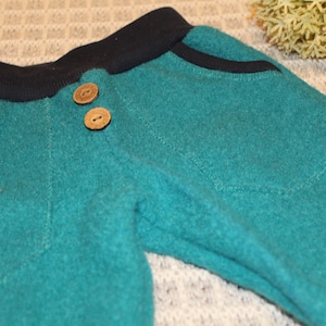 May include: Teal blue sweatpants with a black waistband and two wooden buttons.