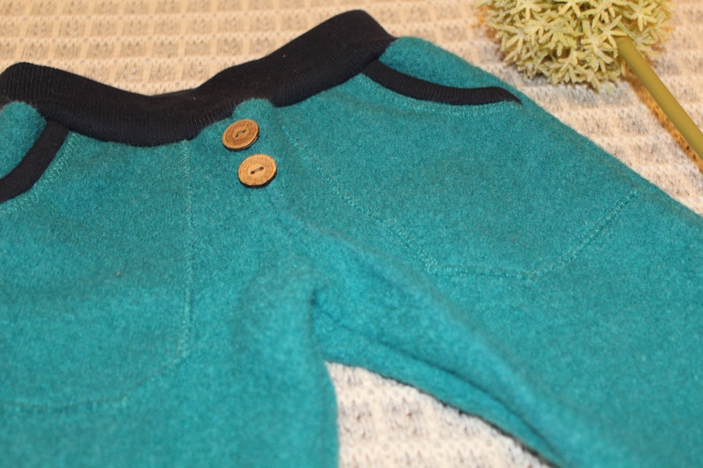 May include: Teal blue sweatpants with a black waistband and two wooden buttons.