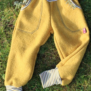 May include: Mustard yellow children's pants with striped cuffs and pockets. The pants are made of a soft, fuzzy fabric.