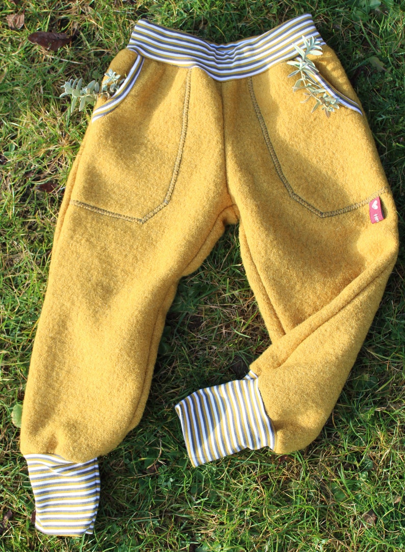 May include: Mustard yellow children's pants with striped cuffs and pockets. The pants are made of a soft, fuzzy fabric.