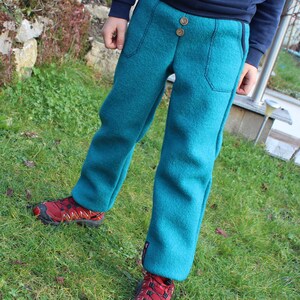 May include: A child wearing teal blue fleece pants with a button fly and side pockets. The pants are worn with red sneakers.