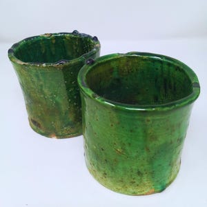 May include: Two green ceramic pots with a speckled glaze. The pots are cylindrical in shape and have a slightly flared rim.