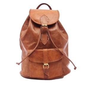 May include: A brown leather backpack with a flap closure and a front pocket. The backpack has a drawstring closure and a top handle. The leather has a distressed look, and the hardware is gold-colored.