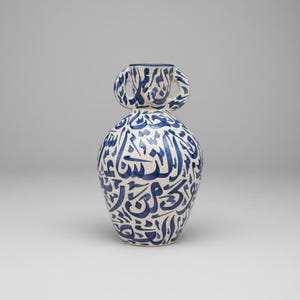 Puede incluir: Jarrón de cerámica blanco con caligrafía azul. Tiene un cuerpo bulboso y dos asas en la parte superior. El borde y las asas son azules. La superficie presenta una textura craquelada.