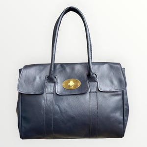 May include: A navy blue leather handbag with a gold clasp. The bag features two handles and a flap closure. The rectangular bag has a structured design, suitable for everyday use.