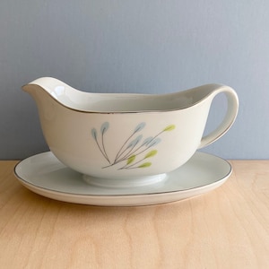 May include: A white ceramic gravy boat with a blue and green floral design. The boat has a matching saucer.