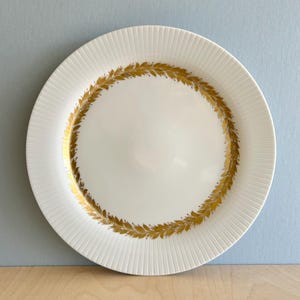 Può includere: Piatto da portata in ceramica bianca con un motivo a foglie dorate intorno al bordo.