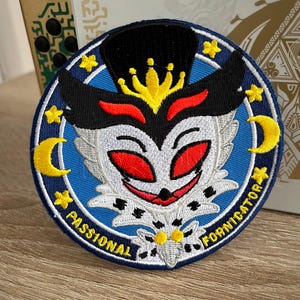 May include: Embroidered patch featuring a stylized owl design with red eyes, a black top hat, and a yellow crown. The patch is circular, with a blue background and the words "PASSIONAL FORNICATOR" in white.