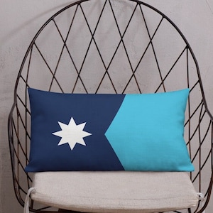 Puede incluir: Una almohada azul y turquesa con una estrella blanca en el centro. La almohada está sentada en una silla de metal negro con un cojín blanco.