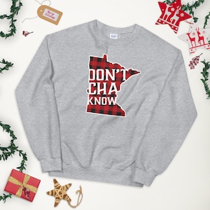 May include: Grey sweatshirt featuring a red and black checked outline of the state of Minnesota. The text "Don't Cha Know" is printed in white within the outline.