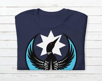 May include: Navy blue t-shirt featuring a graphic of a black bird with a red eye, white dots, and light blue wings, set against a white starburst. The bird design is centered on the shirt.