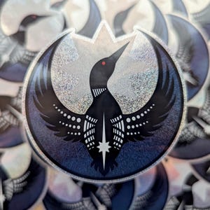 May include: A holographic sticker depicting a black bird with outstretched wings, a red eye, and a star. The bird is set against a crescent moon shape with a silver and blue gradient background. The sticker has a shiny, reflective surface.