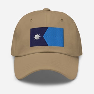 May include: A tan baseball cap with an embroidered blue and navy flag featuring a white star. The flag is centered on the front of the cap.