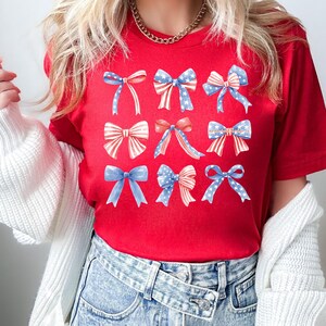 Puede incluir: Camiseta roja con un patr&oacute;n de nueve lazos azules y rojos con estrellas blancas. Los lazos est&aacute;n dispuestos en tres filas de tres.