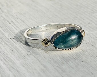 May include: A silver ring featuring a teardrop-shaped green gemstone set in a textured silver bezel. The ring is accented with two small gold beads.