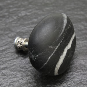 Pode incluir: Botão de mármore preto e branco com base de metal prateado. O botão é redondo e tem um acabamento liso e polido.