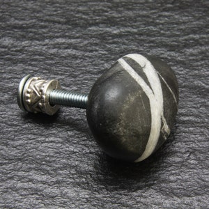 May include: Black and white stone knob with a silver metal base. The knob is attached to a screw.