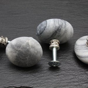 Könnte beinhalten: Drei graue Steintürgriffe mit silbernen Metallakzenten und Schrauben. Der Stein hat ein marmoriertes Muster.
