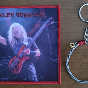 May include: Red square patch with a white border featuring a photo of a musician playing a bass guitar. The musician is wearing a black shirt and has long blonde hair. The text "ALEX WEBSTER" is printed in white at the top of the patch.