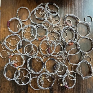 Può includere: Una collezione di portachiavi in corda di chitarra argentata. I portachiavi sono realizzati con corde di chitarra intrecciate e presentano una varietà di colori e design.