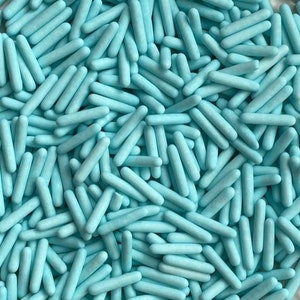 May include: A close-up image of a large quantity of light blue sprinkles. The sprinkles are long and thin, resembling small sticks.