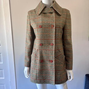 May include: A vintage green and orange plaid coat with a double-breasted design. The coat features a wide collar, two rows of red buttons, and two front pockets. The coat is displayed on a mannequin.