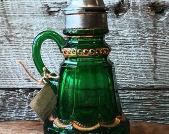 May include: A green glass bottle with a silver lid and gold accents. The bottle has a handle and a label that says "Ewing Bros. 1880-1902".
