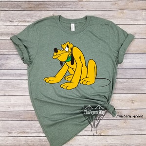 May include: A green t-shirt with a cartoon image of Pluto, a yellow dog with a green collar, looking angry. The text "The Pryces Way" and "military green" are visible in the bottom right corner of the image.