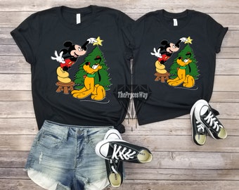 May include: Black t-shirts with a graphic of Mickey Mouse and Pluto decorating a Christmas tree. The text "The Pryces Way" is visible on the bottom right of the image.