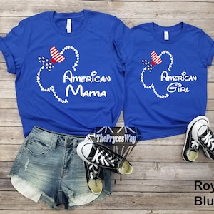 May include: Two royal blue t-shirts with a white outline of Mickey Mouse's head and ears. The ears are filled with red, white, and blue stars and a red bow. The text "American Mama" and "American Girl" is printed on the shirts.