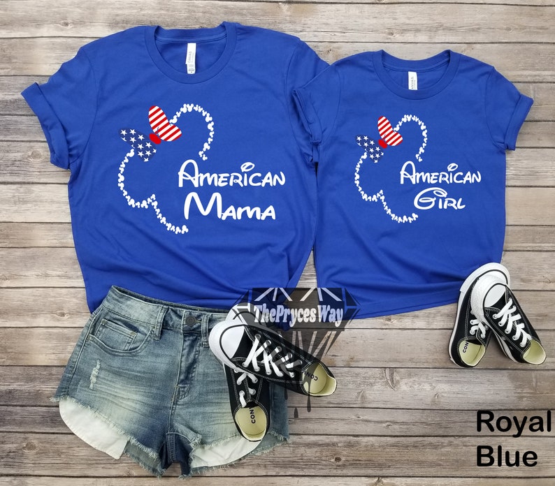 May include: Two royal blue t-shirts with a white outline of Mickey Mouse's head and ears. The ears are filled with red, white, and blue stars and a red bow. The text "American Mama" and "American Girl" is printed on the shirts.