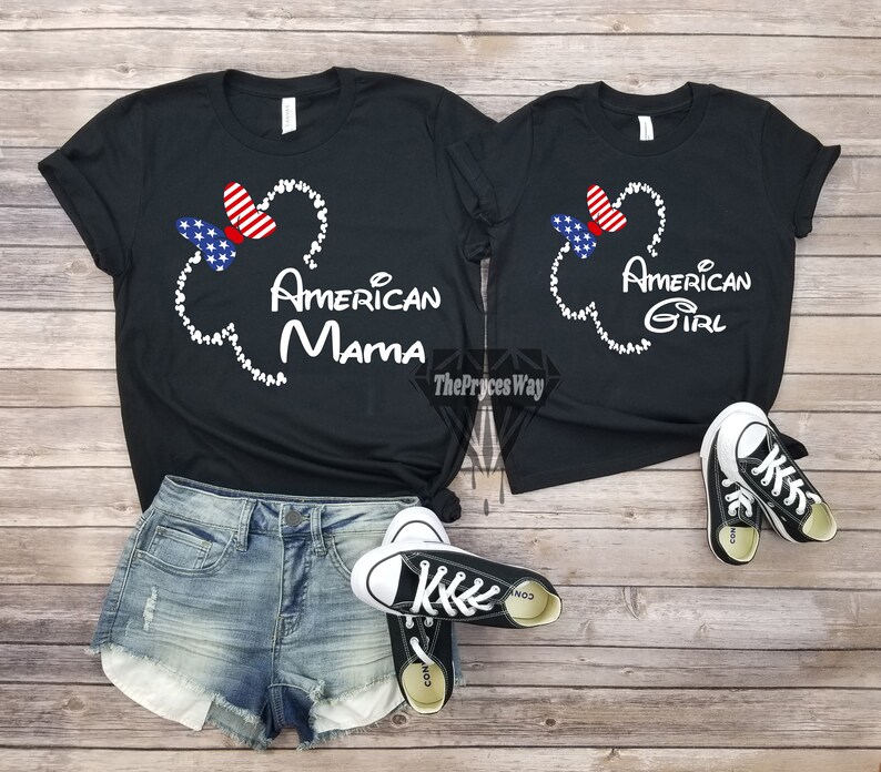 May include: Two black t-shirts with a white Mickey Mouse head outline and a red, white, and blue bow. The larger shirt says "American Mama" and the smaller shirt says "American Girl".