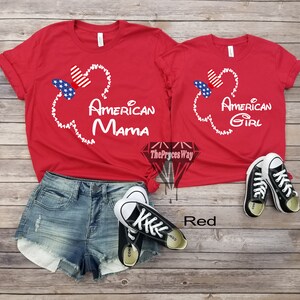 May include: Red t-shirts with a white Mickey Mouse head design and the text "American Mama" and "American Girl". The shirts are on a wooden surface with a pair of black Converse shoes.