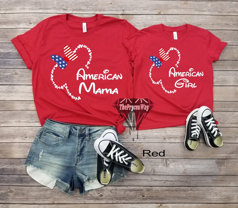 May include: Red t-shirts with a white Mickey Mouse head design and the text "American Mama" and "American Girl". The shirts are on a wooden surface with a pair of black Converse shoes.