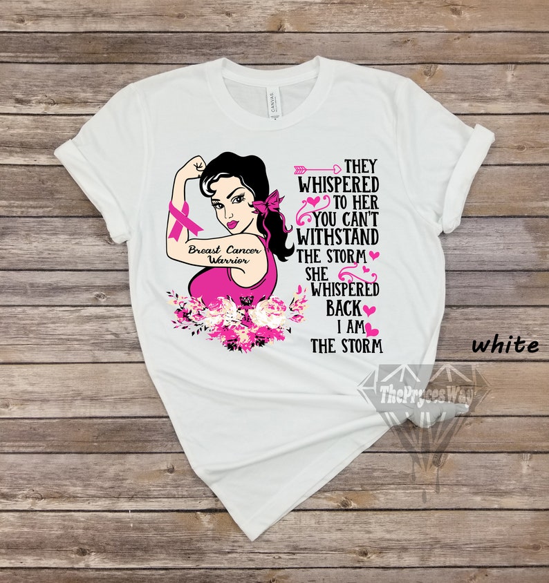 Pu&ograve; includere: Maglietta bianca con una grafica rosa di una donna con un nastro rosa, fiori e il testo "Breast Cancer Warrior" e "They whispered to her you can't withstand the storm. She whispered back I am the storm."
