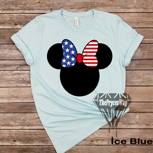 May include: A light blue t-shirt featuring a black Mickey Mouse head silhouette. The bow on Mickey's head is red, white and blue with a stars and stripes pattern. The text "The Pryces Way" is printed on the bottom right corner of the shirt. The text "Ice Blue" is printed below the shirt.