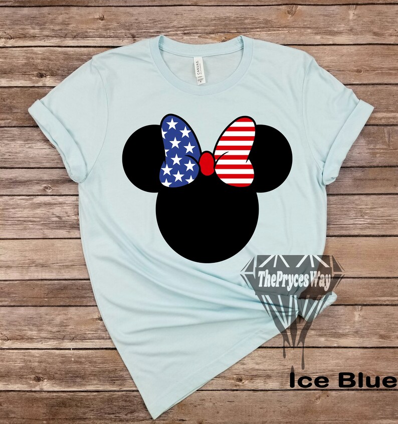 May include: A light blue t-shirt featuring a black Mickey Mouse head silhouette. The bow on Mickey's head is red, white and blue with a stars and stripes pattern. The text "The Pryces Way" is printed on the bottom right corner of the shirt. The text "Ice Blue" is printed below the shirt.