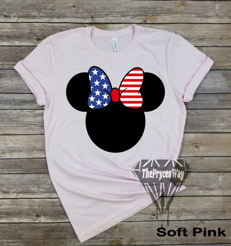 May include: A soft pink t-shirt featuring a black Mickey Mouse head design. The bow on Mickey's head is red, white and blue with a pattern of stars and stripes, resembling the Union Jack.