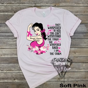 Pu&ograve; includere: Maglietta rosa con una grafica di una donna con un nastro rosa e il testo "Breast Cancer Warrior". Il testo "They whispered to her you can't withstand the storm. She whispered back I am the storm." &egrave; anche sulla maglietta.