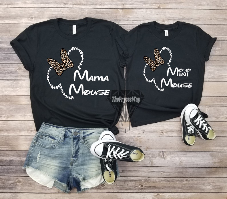Może przedstawiać: Dwie czarne koszulki z białym obrysem uszu Myszki Miki i kokardką w panterkę. Większa koszulka ma napis "Mama Mouse", a mniejsza "Mini Mouse".