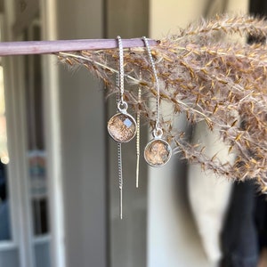 May include: A pair of silver chain earrings with small round clear glass beads that have a gold fleck inside.